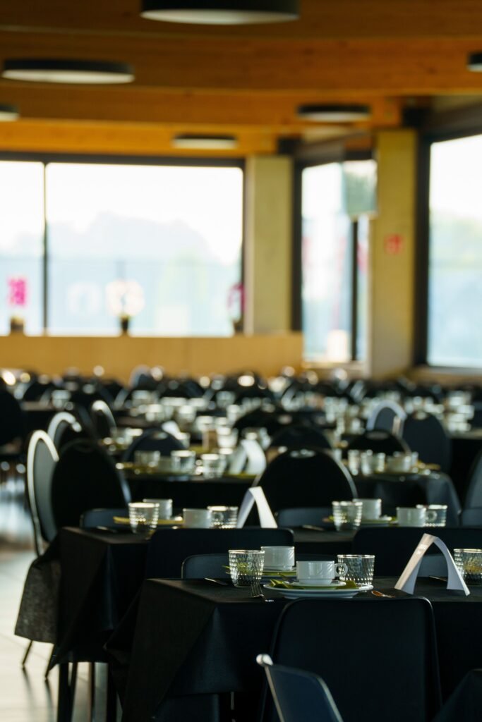 A spacious and elegant banquet hall with neatly arranged black-draped tables and glassware.